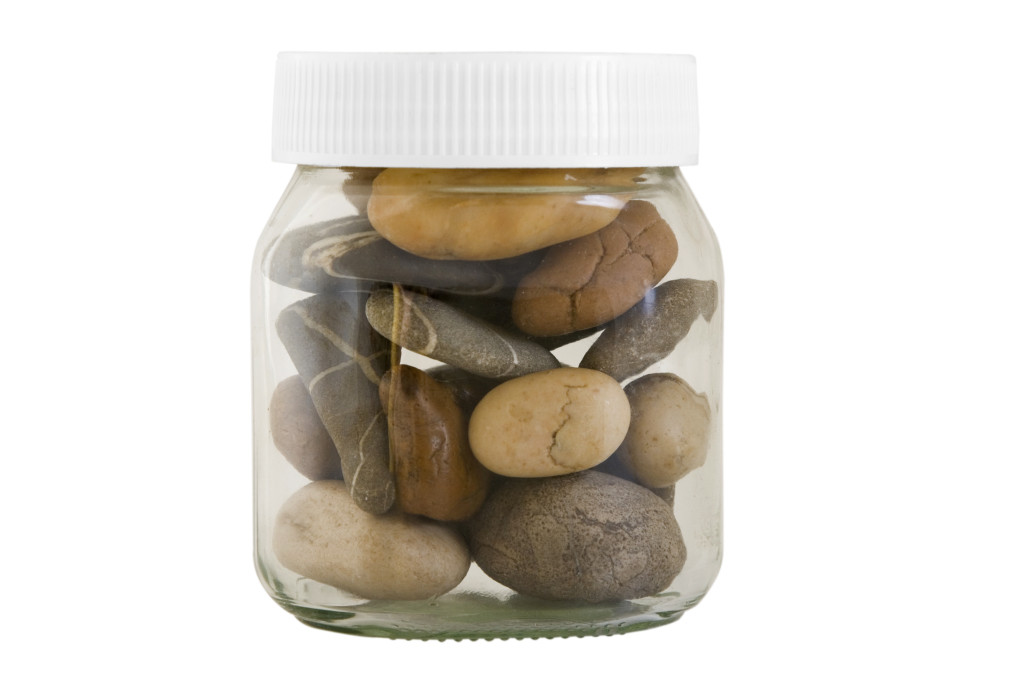 transparent jar with different stones on white background